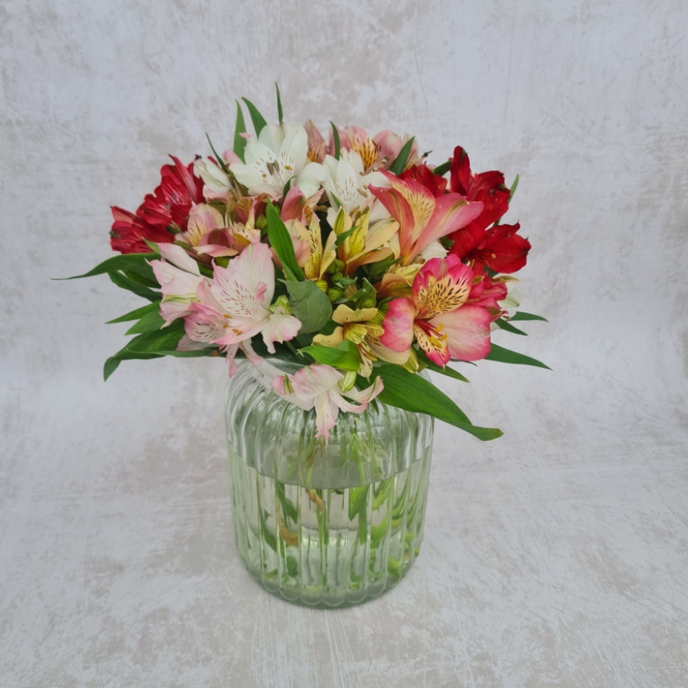 Vibrant multi-colored alstroemeria flower bouquet arranged in a sustainable glass vase on a bright countertop.
