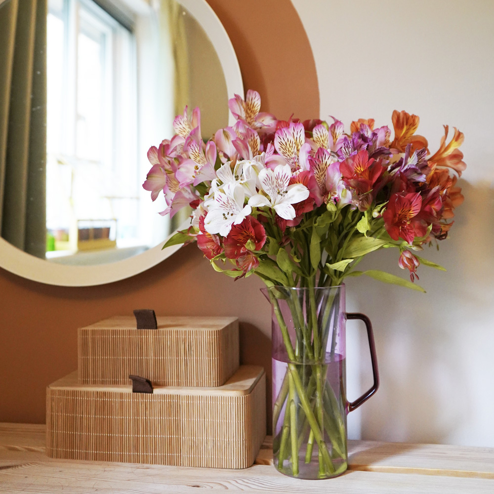 Vase of mixed alstroemeria on shelf with mirror in background